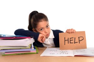 sweet little female latin child studying on desk lasking for help in stress with a tired face expression in children education and back to school concept isolated on white background