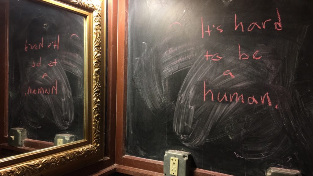 Chalkboard with "Its hard to be a human" written on it, and a mirror reflecting the chalkboard.